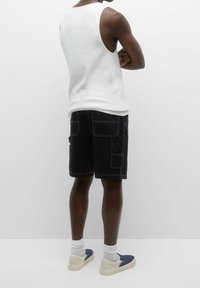 Débardeur blanc, short cargo noir avec multiples poches, et chaussures bleues à enfiler. Fond uni, met en valeur le design et la coupe des vêtements.