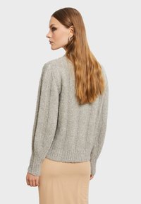 Šedý pletený svetr s vroubkovanou texturou, spadlými rameny a zkráceným lemem. Nositý přes béžovou sukni. Dlouhé vlasy padající na záda.