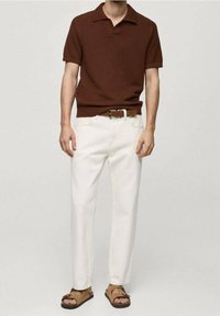 Polo de punto marrón de manga corta con cuello, combinado con pantalones rectos blancos y sandalias marrones. Estilo casual, ajuste relajado.