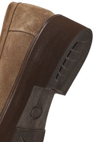 Bruine leren laars met een gestructureerde donkerbruine rubberen zool, met een gebogen vorm en subtiele stikdetails. Flexibel materiaal accent.