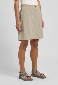 Gonna khaki a metà coscia realizzata in tessuto leggero, caratterizzata da una cucitura frontale e una chiusura con un singolo bottone in vita. Sandali con dettagli a motivo.