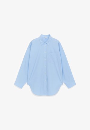 Camisa azul claro de manga larga con botones, cuello puntiagudo y bolsillo en el pecho, mostrada desplegada sobre un fondo blanco.