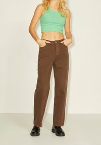 Brown corduroy pants feature a straight-leg design, front pockets, and a button closure. Paired with a green cropped top and black shoes.