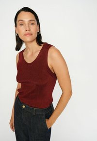 Bordeaux zonder mouwen ribbeltop met een ronde halslijn, gecombineerd met donkerblauwe denim jeans. De outfit heeft een relaxte pasvorm.