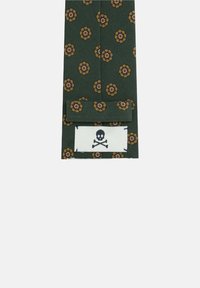 Accesorio de tela verde con patrones florales en amarillo y rojo, con una etiqueta blanca que muestra un diseño de calavera y tibias cruzadas en negro.