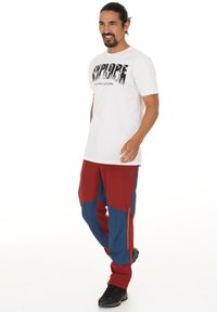 Valkoinen t-paita, jossa on teksti "EXPLORE", yhdistetty punaisiin ja sinisiin monitoimihousuihin, joissa on sivuvetoketju ja teksturoitu kangas. Mustat saappaat.