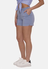 Pantaloni corti blu chiaro con vestibilità su misura, dotati di tasche laterali e una leggera apertura all'orlo, abbinati a sneakers bianche.