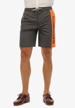 Shorts de bain gris avec un panneau latéral orange arborant "SUPERDRY." Tissu léger, taille élastique et cordon de serrage.