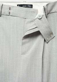Pantalon gris clair à fines rayures, avec bouton, fermeture éclair et passants de ceinture, montrant la ceinture et l'étiquette de marque MNG à l'intérieur.
