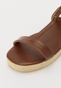 Brown leather sandal featuring two upper straps, a rounded toe, and a textured jute sole for added grip and comfort.