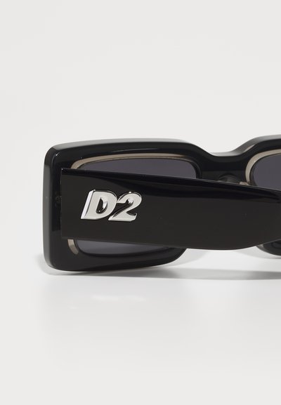 Svarta, översized solglasögon med fyrkantiga bågar, mörka linser och silverfärgad logotyp "D2" på utsidan av armen. Slät plaststruktur.