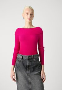 Haut rose à côtes ajusté avec un col asymétrique, manches longues, associé à une jupe en denim foncé taille haute.