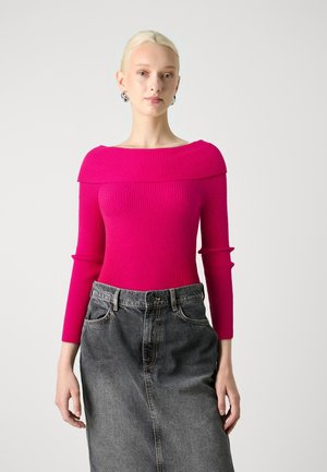 Top rosa a coste, aderente, con scollo a spalla scoperta e maniche lunghe, abbinato a una gonna di jeans scura a vita alta.