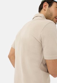 Beige polo shirt met een klassieke kraag en korte mouwen, voorzien van een textuurstof en een ontspannen pasvorm.