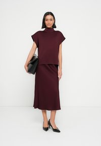 Ensemble bordeaux deux pièces composé d'un haut à col roulé à manches courtes et d'une jupe fluide. Texture lisse, assorti à des talons noirs et une pochette.