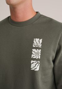 Olijfgroene sweatshirt met een ronde hals en drie witte bloemenprints aan de linkerkant. Gemaakt van zachte, gestructureerde stof.