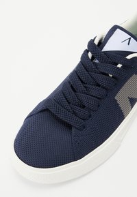 Zapatilla de malla azul marino con punta redonda y superficie texturizada, que cuenta con cordones planos y una suela de goma blanca. Diseño de plantilla extraíble.