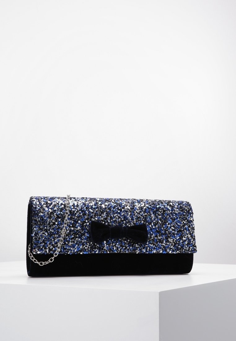 Pochette rectangulaire noire et bleue pailletée avec bandoulière chaîne argentée et nœud en velours noir à l'avant, exposée sur un socle blanc.