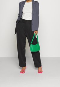 Szara marynarka, biały top z teksturowaną lamówką, czarne spodnie o szerokich nogawkach, zielona torebka z fakturą krokodyla, różowe sandały na paski.