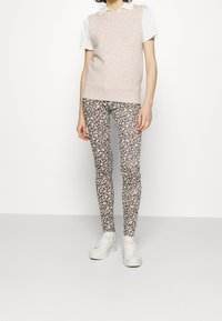 Suéter sin mangas color beige claro sobre una camisa blanca con cuello, combinado con pantalones ajustados de patrón floral y zapatillas de plataforma blancas.
