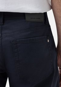 Dunkelblaue Denim-Hosen mit strukturiertem Finish, ausgestattet mit einer rechteckigen Gesäßtasche, einem Leder-Logo-Patch und Kontrastnähten.
