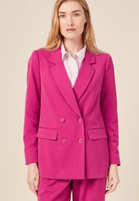 Fuchsia dubbelzijdig blazer met een gekartelde kraag, twee voorkeurszakken en accenten van zilverkleurig hardware, gecombineerd met een licht gestreept shirt.