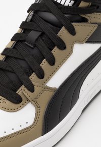 Sneakers med en blandning av material: svart läder, olivgröna Accenter, vit mellansula och texturerade svarta snören. Designen har sportiga detaljer.