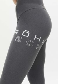 Schwarze Leggings aus einem glatten, dehnbaren Material, die auf dem linken Bein weißen Drucktext und geschwungene Nahtdetails aufweisen.