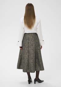 Ilga, raštuota sijonas su tamsiai pilku pagrindu ir šviesiais gėlių akcentais, derinama su balta marškinėliais, turinčiais kontrastingus rankogalius ir juodus mygtukus.