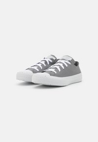 Para niskich szarych sneakersów z płótna z białymi gumowymi podeszwami i białymi sznurówkami na białym tle.