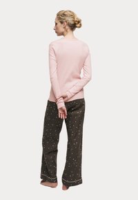 Top de manga larga rosa claro con un escote redondeado, combinado con pantalones verdes oscuros con un estampado de estrellas blancas, de tela suave y corte relajado.