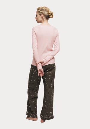 Top a maniche lunghe rosa chiaro con scollatura rotonda abbinato a pantaloni verde scuro con pattern di stelle bianche, tessuto morbido, vestibilità rilassata.