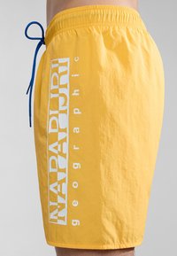 Geel zwembroek met een elastische tailleband en een blauwe trekkoord. Bevat een witte bedrukte logo aan de zijkant. Lichtgewicht, gladde textuur.