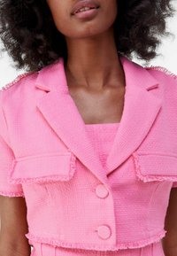 Pink textured blazer with short sleeves, featuring frayed edges, two front pockets, and button fastenings. Balanced contemporary design.