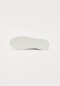 Semelle de chaussure en caoutchouc blanc avec un motif de grip texturé et un bord lisse. Présente une empreinte rectangulaire près du centre.