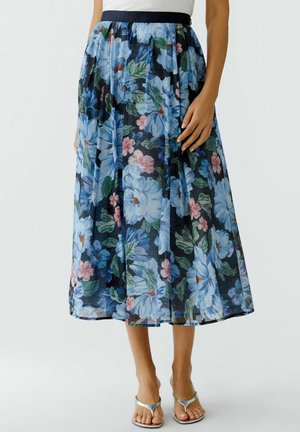 Midirock mit großem blauem und pinkem Blumenmuster, kombiniert mit silbernen Sandalen mit offenen Zehen und weißem Oberteil, Fokus auf unteren Körperbereich und Hand.