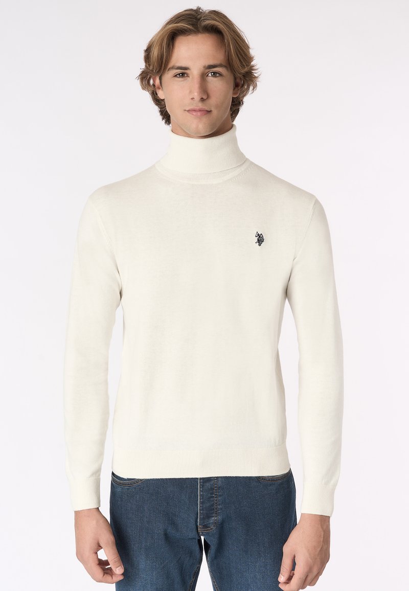 Maglione bianco a collo alto con polsini e fondo a coste. Presenta un piccolo logo nero sul lato sinistro del petto. Tessuto morbido, design aderente.