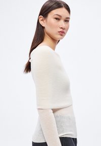 Svetložltý sveter s dlhými rukávmi a priliehavým strihom. Mäkká textúra a bezšvový dizajn, s širokým výstrihom a vrstveným efektom v oblasti pása.