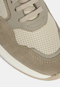 Sneaker en daim marron avec des panneaux en cuir beige perforé, lacets plats beige et semelle en caoutchouc blanche. Design courbé avec des détails de couture.
