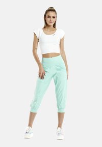Pantaloni jogger cropped verde menta con cintura elasticizzata, dotati di tasche laterali e polsini elasticizzati, abbinati a una maglietta bianca aderente e sneakers multicolori.