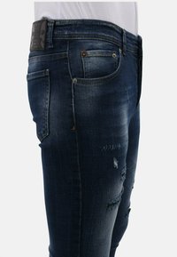 Diepblauwe denim jeans met een slim fit, voorzien van verschoten details en meerdere zakken. De tailleband heeft een zwart leren label.