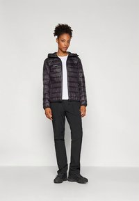 Crna pufasta jakna s kapuljačom, prošivenim uzorkom i prednjim patentnim zatvaračem, u kombinaciji s crnim hlačama i tamnom obućom. Ispod je bijela košulja.