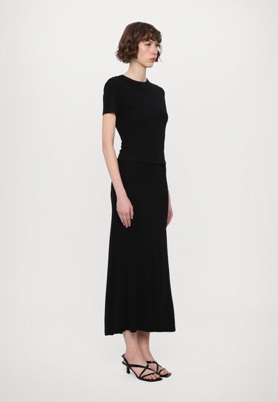 Black fitted top paired with a long, flowing black skirt. The material appears soft and smooth, with minimal design details and short sleeves.