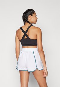 Svart idrotts-bh med korsade band, parat med vita shorts med blå kant. Slät tyg, åtsittande design, med hög midja.
