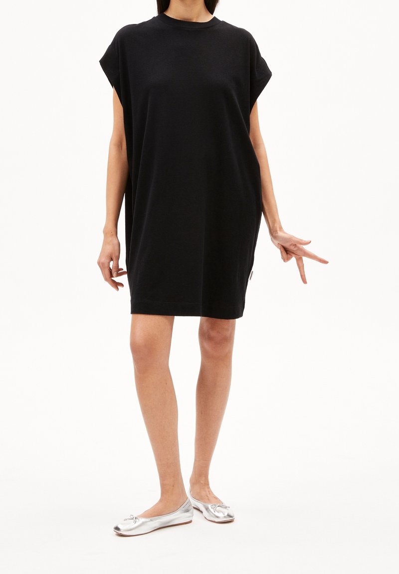 Robe oversize en coton noir avec des manches courtes, un col rond et une coupe décontractée. Portée avec des ballerines argentées pour un look décontracté.