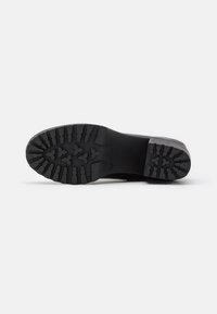Semelle de chaussure noire avec un motif de semelle profond comportant des formes triangulaires et rectangulaires, talon plat et construction robuste.