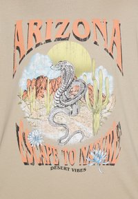 Beige t-shirt featuring a graphic design of a coiled snake, cacti, and mountains, with "ARIZONA" and "ESCAPE TO NATURE" text in orange and black.