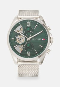 Silver mesh strap watch with a green textured dial, silver hour markers, date and day indicators, and a visible movement window.