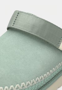 Ανοιχτό πράσινο παπούτσι από υλικό με υφή, με λουράκι και διακοσμητικό ράψιμο κατά μήκος της άκρης, με απαλό, ματ φινίρισμα.