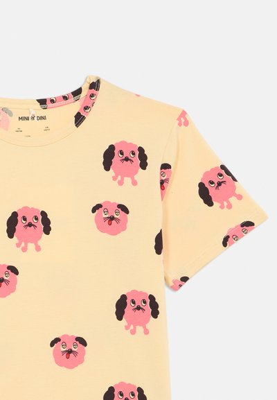 Beige, rövid ujjú ing pink színű, ismétlődő mese kutya arcokkal, fekete fülekkel és kifejező szemekkel az anyagon.